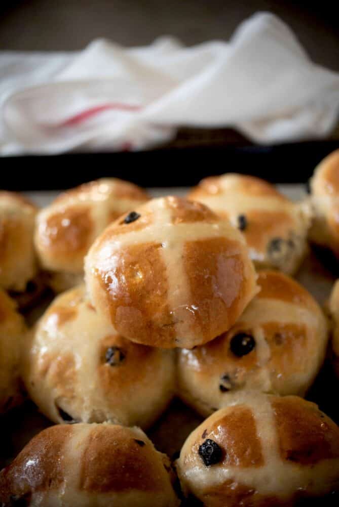 One hot cross bun on top of a tray of hot cross buns
