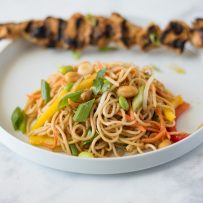 Noodle salad on a white plate with grilled chicken skewer