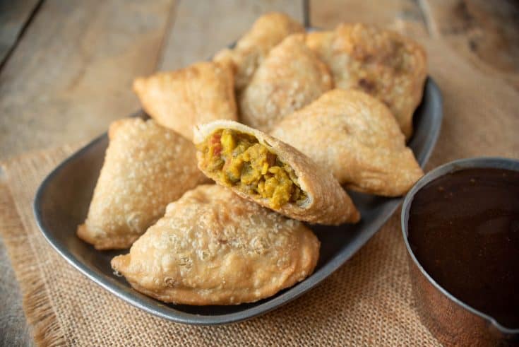 A cut open samosa showing the lentil curry filling laying on a plate with other samosa