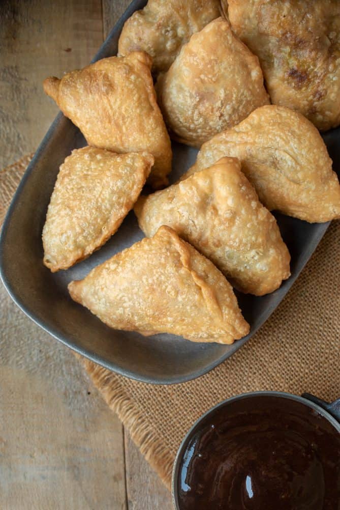 Samosa viewed from overhead spread out onto a grey plate with a side of dark colored tamarind date chutney