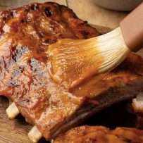 A closeup of brushing the ribs with mango barbecue sauce
