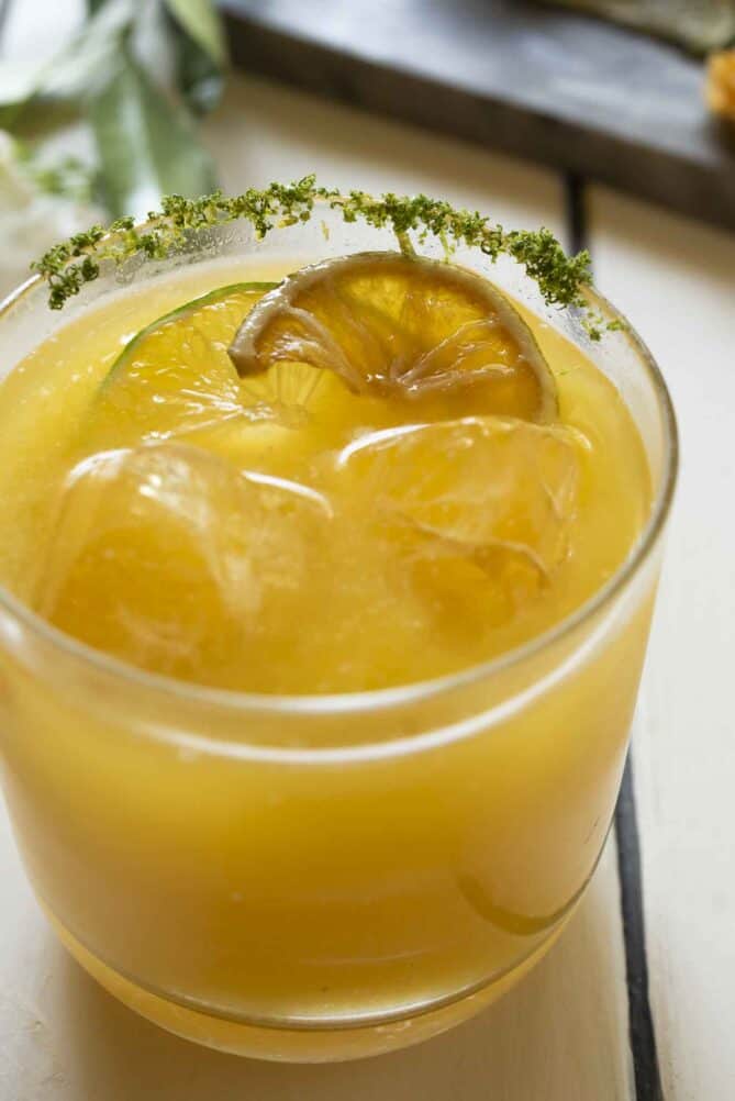 A bright orange glass of juice over ice cubes