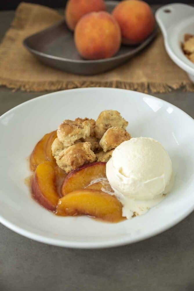 A scoop of vanilla ice cream with sliced peaches and cobbler crust