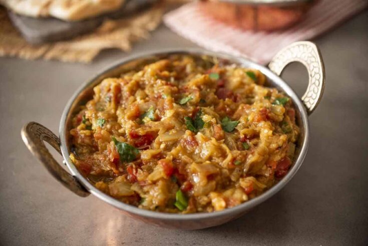 A round copper bowl with handles filled with mashed Indian eggplant and cilantro