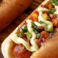 A juicy hot dog in a bun topped with pinto beans, salsa and avocado crema