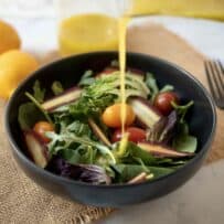 Pouring Meyer lemon vinaigrette over a colorful salad