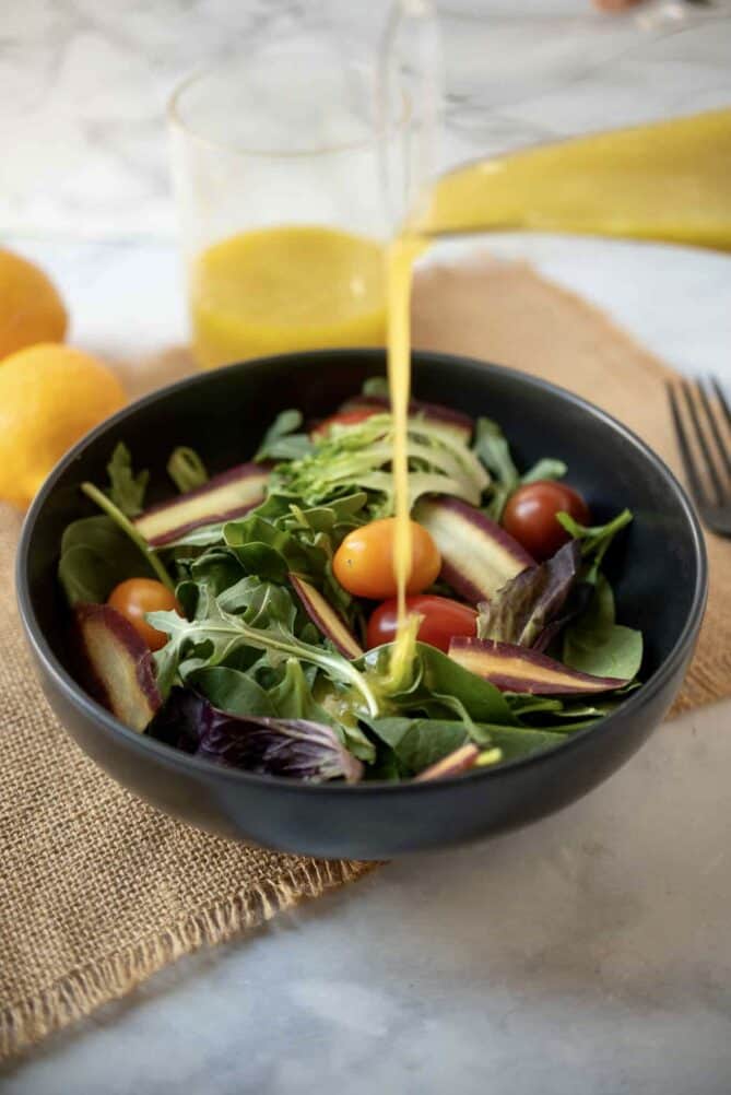 Pouring Meyer lemon vinaigrette over a colorful salad