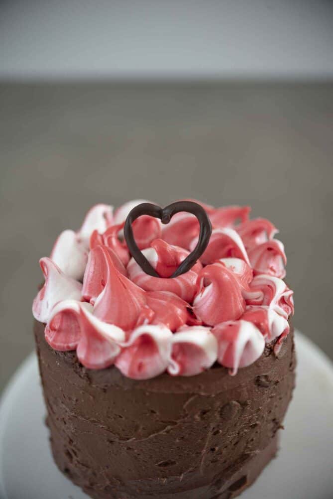 A chocolate heart on top of a cake decorated with red and white frosting