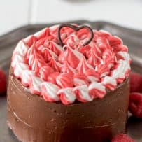 A small chocolate cake coated on the sides with chocolate frosting and red and white frosting on the top.