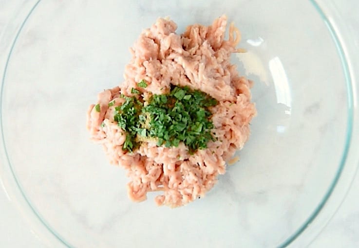 Ground chicken in a glass bowl with fresh mint, cilantro and spices