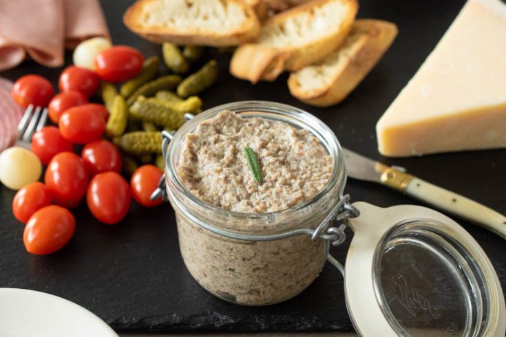 A jar of mushroom p&acirc;t&eacute; on a slate board with cherry tomatoes, cheese and bread