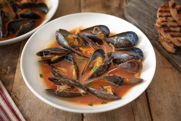 A large bowl of mussels in tomato broth with grilled bread