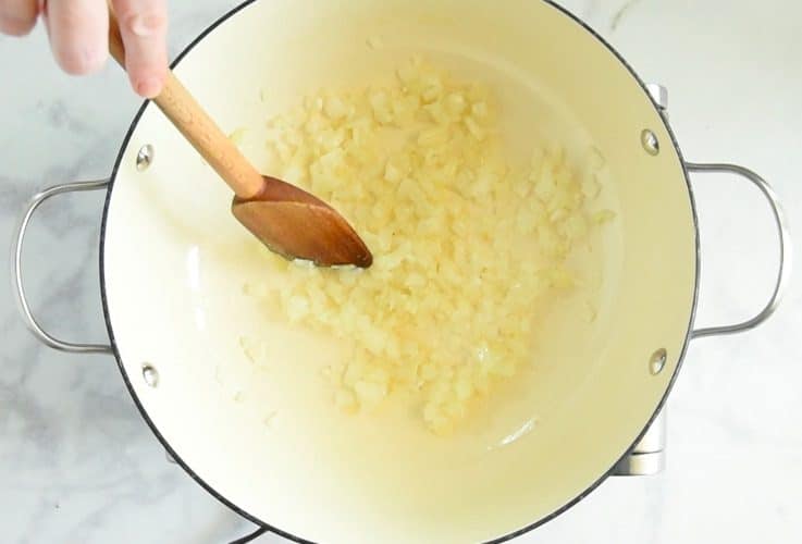 Onions and garlic being sauteed in a pan being stirred with a wooden spoon