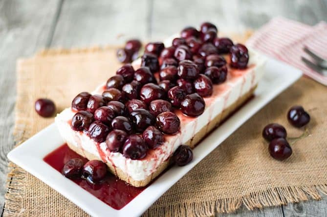 A rectangle shaped no bake cherry cheesecake topped with whole fresh cherries
