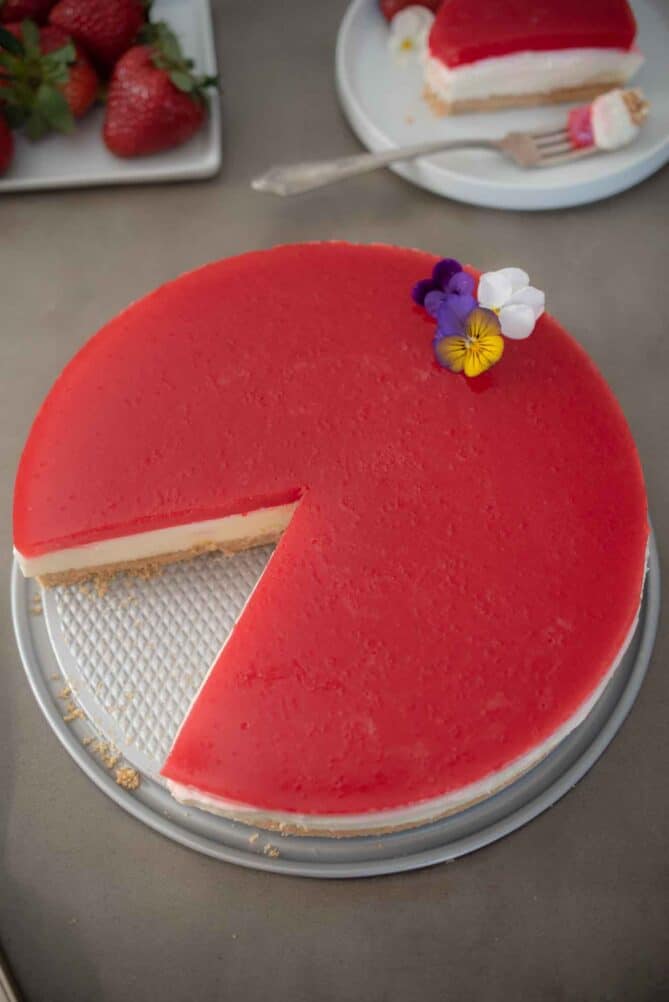 A vibrant red strawberry cheesecake decorated with edible pansy flowers