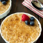 A rice pudding in a white ramekin with a bruleed sugar top with a raspberry and blueberries