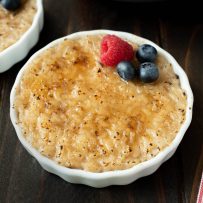 A white bowl of rice pudding with a raspberry and blueberries