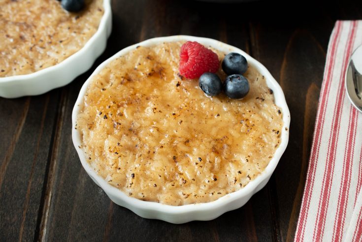 A white bowl of rice pudding with a raspberry and blueberries