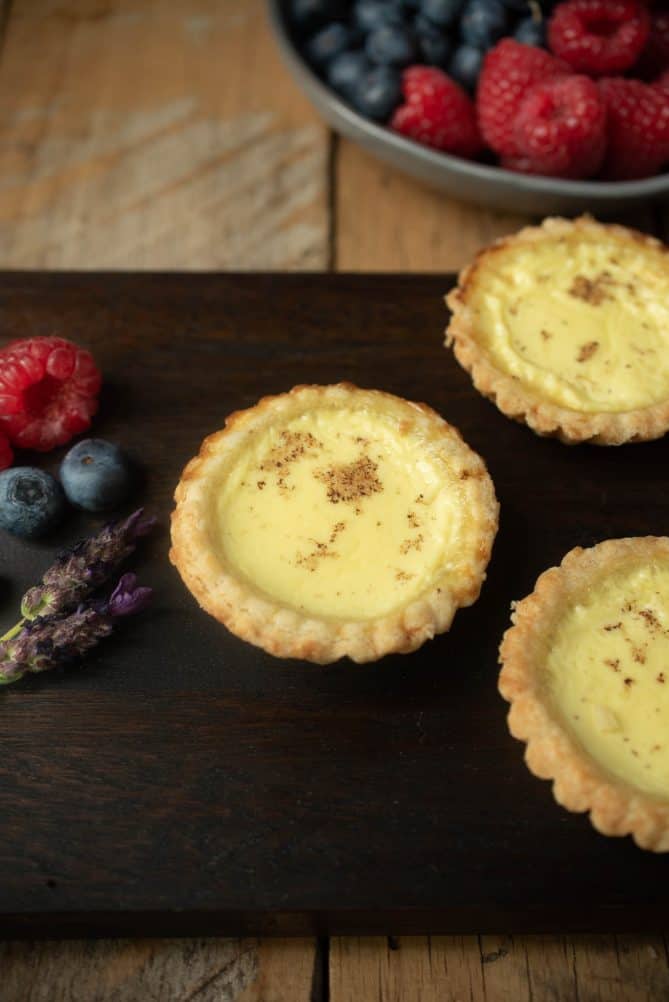 Small egg custard tarts on a presentation board with fresh lavender and berries for garnish