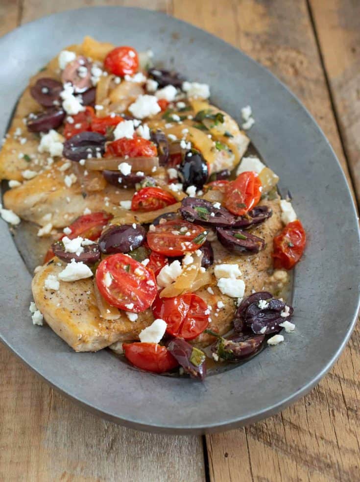 A closeup showing the chicken topped with tomatoes, olives and feta cheese