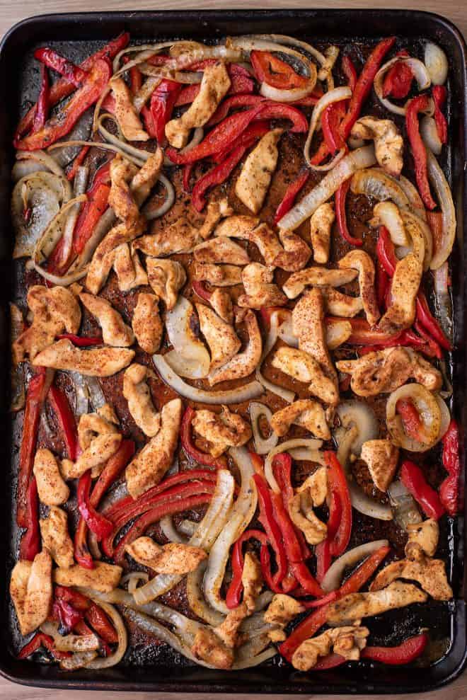A large baking sheet of roasted chicken fajitas with red peppers and onion