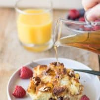Pouring syrup over a piece of French toast casserole with raspberries and blueberries