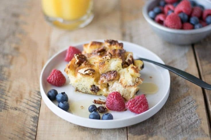 A slice of the French toast casserole on a white plate with blueberries and raspberries
