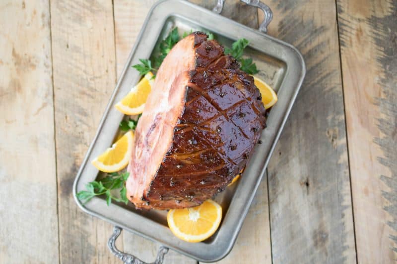 A sliver serving tray with a glazed ham with orange sliced and parsley