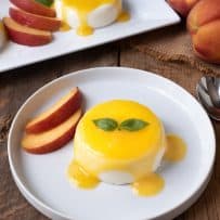 Panna cotta drizzled with peach sauce on a white plate with fresh peach slices