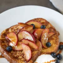 Shiny peach slices cooked in butter and caramel sauce on top of slices of French toast