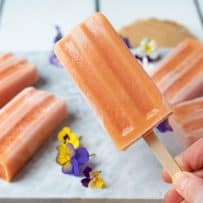 Holding a peach frozen yogurt popsicle with more in the background