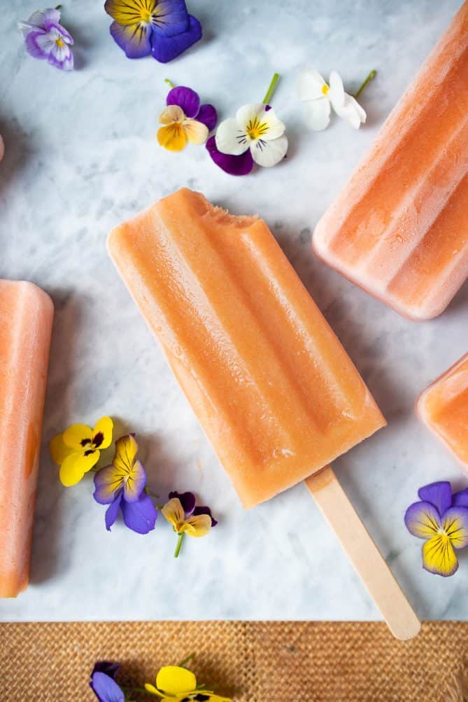 A peach frozen yogurt popsicle with a bite taken from the top right