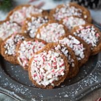 Crushed candy canes on top of lace sandwich cookies displayed on a grey plate