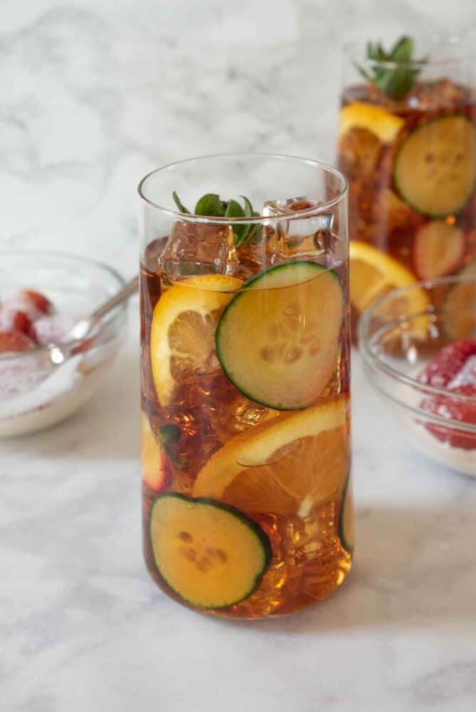 Cucumber and orange slices line the sides of a tall cocktail glass