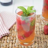 A tall glass of Pimm's strawberry mint cocktail garnished with fresh strawberries and mint