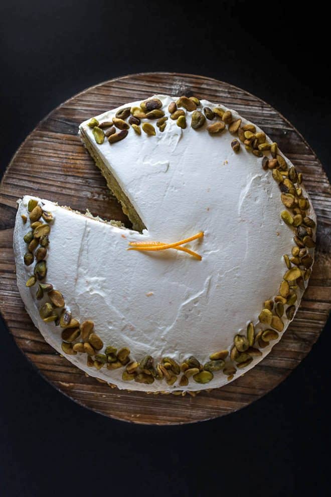 The pistachio cake viewed from overhead with a slice remove and fresh orange garnish