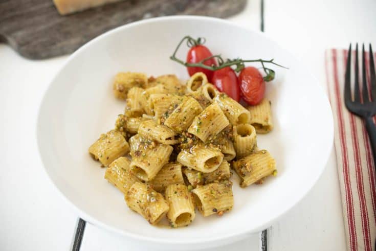 A bowl of pistachio pesto pasta with cherry tomatoes on the vine