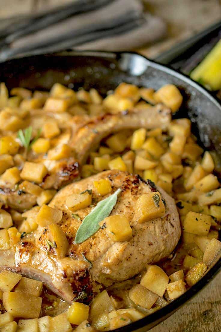 A closeup of a pork chop with chopped apples and sage