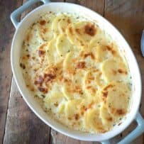 An oval dish of cheesy potato gratin with a large spoon