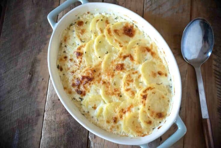 An oval dish of cheesy potato gratin with a large spoon