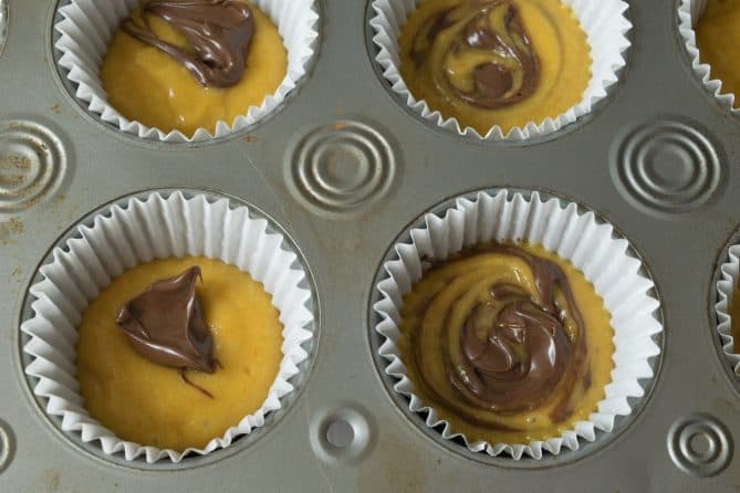 Muffin liners in a muffin pan with pumpkin muffin dough and nutella