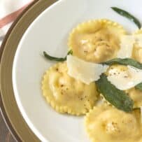 Round ravioli with fluted edges topped with browned butter, crispy sage leaves and shave Parmesan