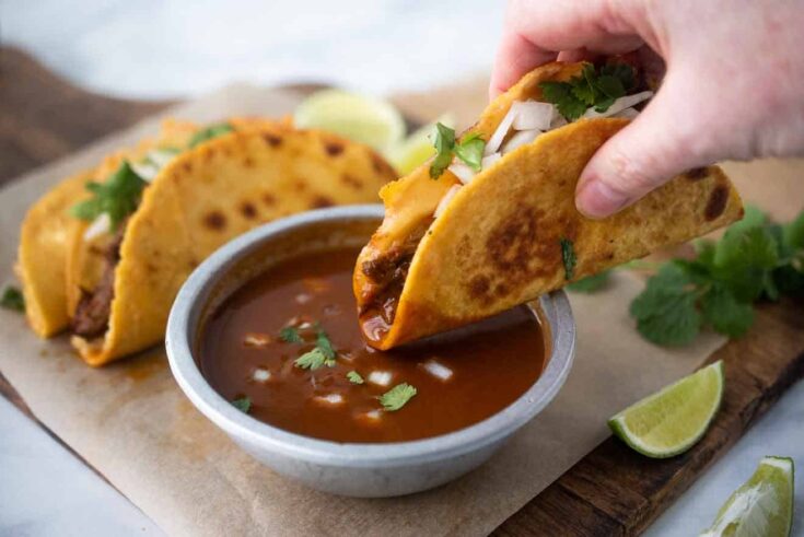 A crispy beef taco being dipped in the sauce used to cook the beef