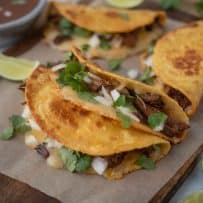 4 beef tacos on a board with fresh lime wedges and cilantro
