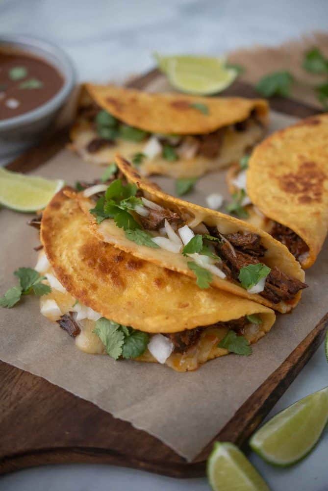 4 beef tacos on a board with fresh lime wedges and cilantro