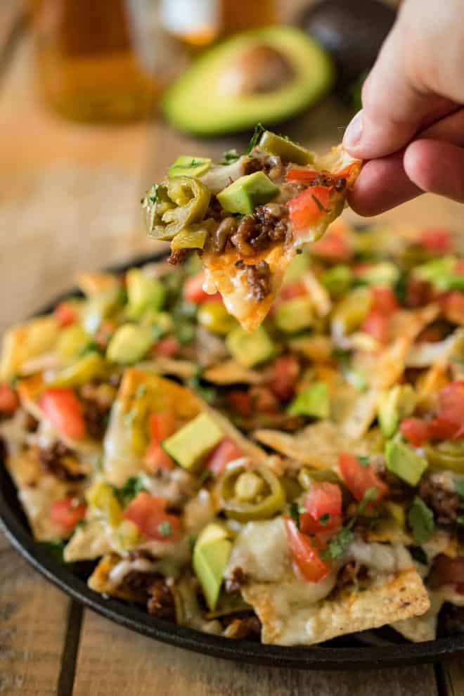 Holding a nacho with cheese, meat, tomato, avocado and avocado