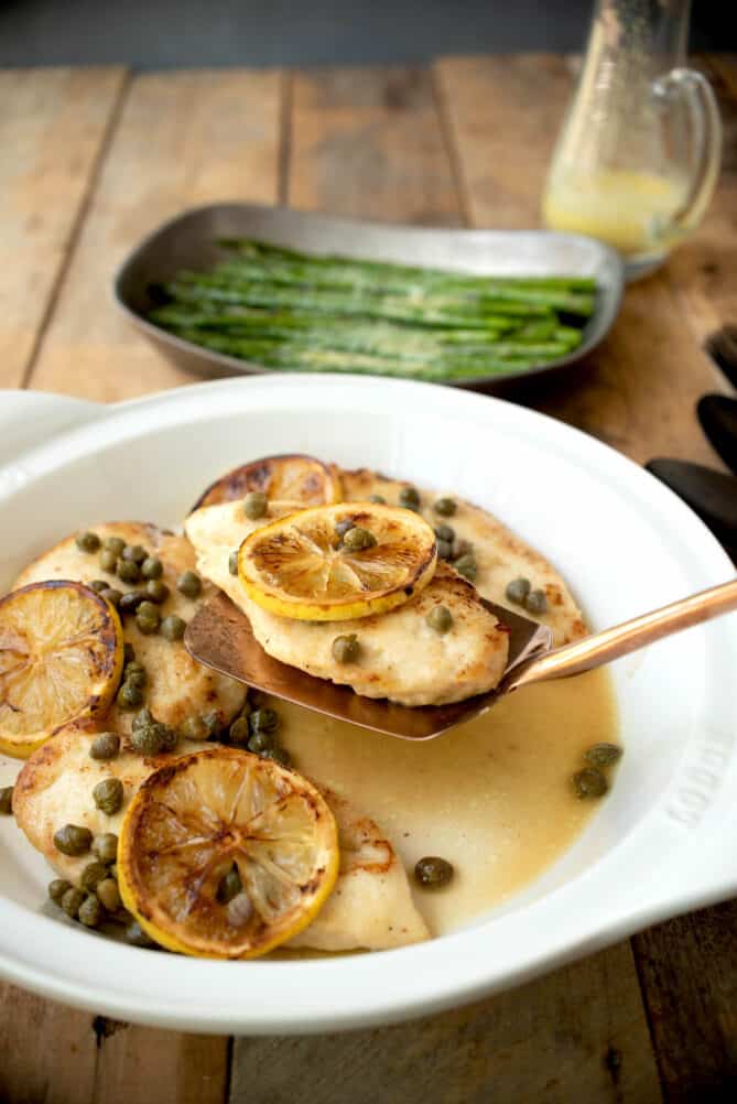 Serving a piece of chicken breast with lemon slice and capers.