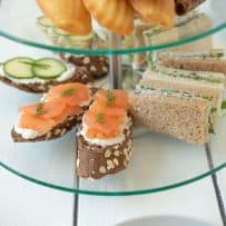 A selection of sandwiches on a tiered tray. Salmon and cream cheese, radish and herb butter