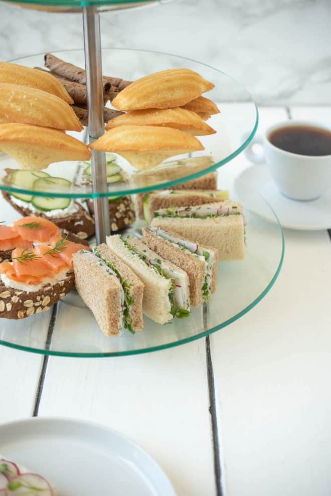 Madeleine cookies and sweet treats in a tiered cake stand with tea sandwiches