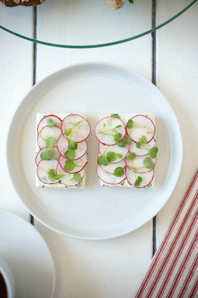 2 open-faced radish and herb butter sandwiches topped with micro greens
